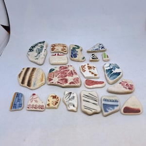 以下が含まれることがあります： 青、緑、赤、白など、さまざまなパターンと色で構成された、18個の小さな壊れたセラミックタイルの断片のコレクションです。