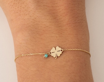 May include: A gold bracelet with a four-leaf clover charm and a turquoise stone accent.