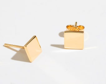 May include: A pair of gold square stud earrings. The earrings have a simple, minimalist design.