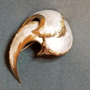 May include: Vintage brooch with a stylized design. The brooch features a curved, claw-like shape with a textured, silver-tone finish and gold-tone accents. The pin is a unique accessory.