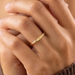 Könnte beinhalten: Ein dünner Goldring mit einer kleinen, flachen, rechteckigen Mittelplatte, in die der Großbuchstabe A eingraviert ist. Der Ring hat eine polierte, reflektierende Metalloberfläche und ein schlichtes, schmales Design, das den Finger umschließt.