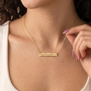 Peut inclure: Un collier doré avec un pendentif rectangulaire. Le pendentif porte l'inscription "Ride Around Gettin' It". Le collier est porté par une personne portant un débardeur blanc.