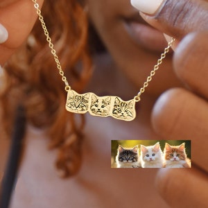 Può includere: Una collana d'oro con tre piccole teste di gatto incise. La collana è indossata da una persona con la pelle scura. Le teste di gatto sono di tre gatti diversi, mostrati in un'immagine più piccola sotto la collana.