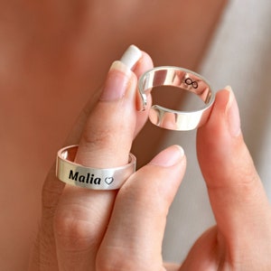 Op de afbeelding: Twee zilveren ringen. Een ring is gegraveerd met de naam "Malia" en een hartje. De andere ring is gegraveerd met een oneindigheidssymbool.