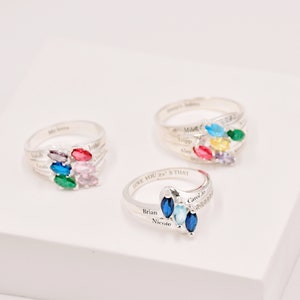 May include: Three silver rings with colorful marquise-cut gemstones. Each ring features a cluster of gems in various colors, including blue, green, pink, and yellow. The rings have engraved names and phrases.