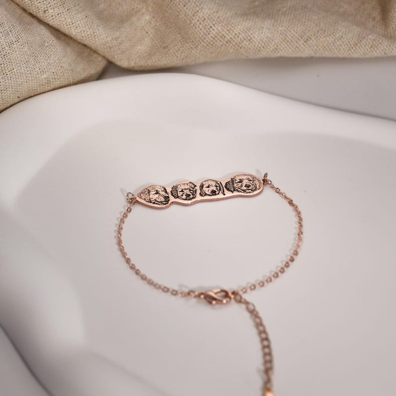 May include: A rose gold bracelet with a charm featuring four engraved dog faces.