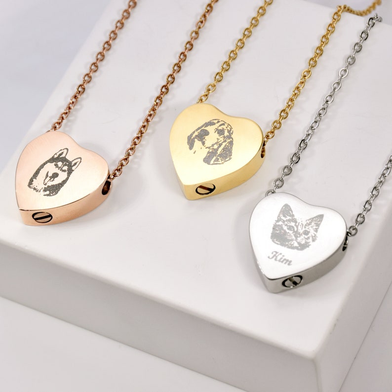 May include: Three heart-shaped pet memorial necklaces in rose gold, gold, and silver. Each pendant features a pet portrait and hangs from a matching chain. The silver necklace has the name "Kim" engraved on it.