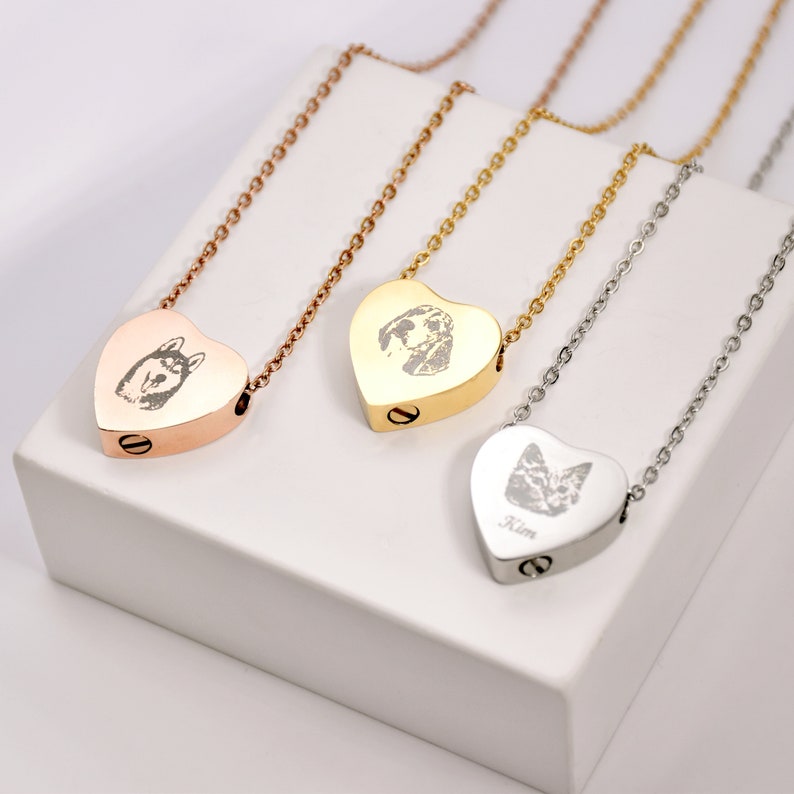 May include: Three heart-shaped pet memorial necklaces. One is rose gold with a dog portrait, another is gold with a dog portrait, and the third is silver with a cat portrait and the name "Kim". Each pendant hangs on a delicate chain.