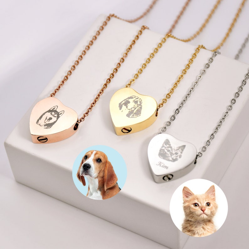 May include: Three heart-shaped pet memorial necklaces in rose gold, gold, and silver. Each pendant has an engraved pet portrait and hangs on a delicate chain. The necklaces are displayed on a white surface.