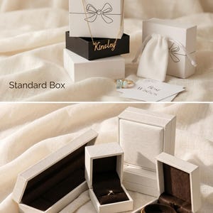 May include: An assortment of jewelry gift boxes in various shapes and sizes. The boxes are white and black, some with a bow design. A gold necklace and rings are visible. The text "Kinsley" is on a black box. The text "Best Wishes" is on a card.