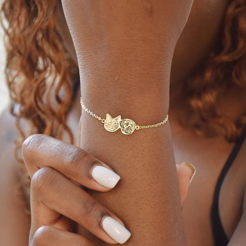 May include: A gold chain bracelet with two round charms featuring the profiles of a cat and a dog.