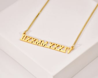 May include: A gold necklace with a bar pendant featuring the Roman numeral date '1994' in a bold, modern font.