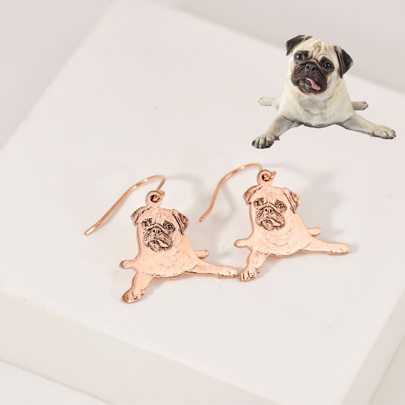 K&ouml;nnte beinhalten: Ohrringe aus ros&eacute;gold mit einem Anh&auml;nger in Form einer Mops-Silhouette. Die Ohrringe sind aus Metall und haben eine gl&auml;nzende Oberfl&auml;che.