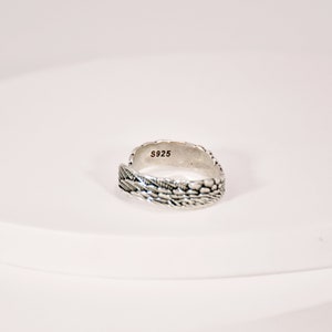May include: A silver ring with a textured design. The ring is marked with the number "S925" on the inside.