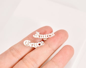 May include: A pair of silver earrings with the names "James" and "Grace" spelled out in a gothic font.