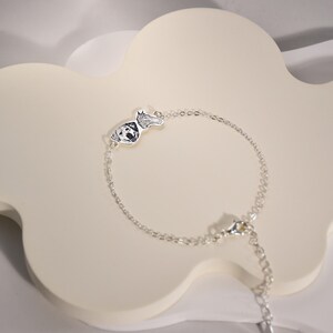 May include: A silver chain bracelet with a small silver charm featuring a dog's paw print and face.