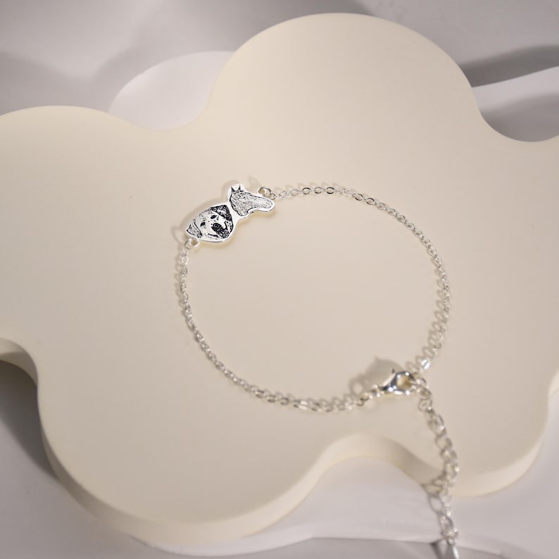 May include: A silver chain bracelet with a small silver charm featuring a dog's paw print and face.