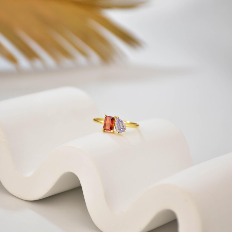 May include: A gold ring with a red rectangular stone and a purple teardrop-shaped stone.