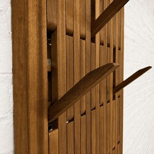 May include: A wall-mounted coat rack constructed from vertical wooden slats in a medium brown tone. The design features multiple retractable hooks that extend outward from the slatted frame, providing functional storage for hanging various items.