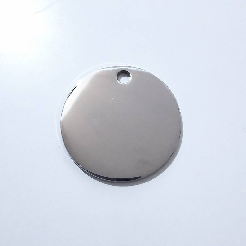 May include: A round, silver-colored metal tag with a hole at the top. The tag is blank and ready to be engraved.