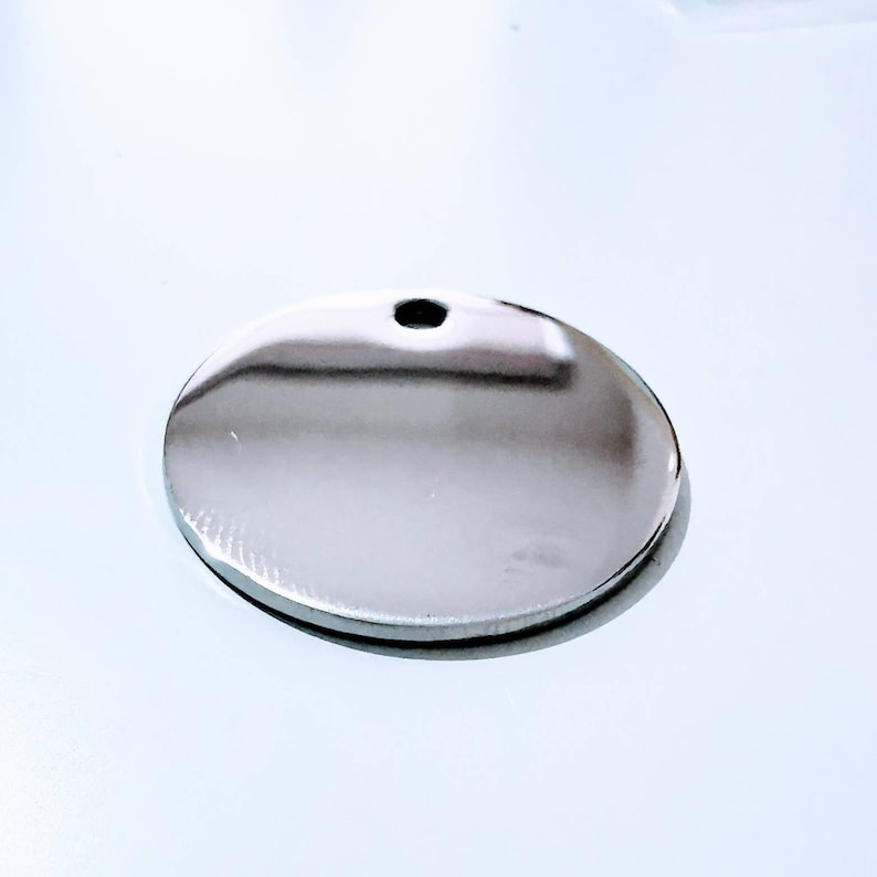 May include: A round, silver-colored metal tag with a small hole at the top.