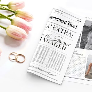 May include: A mock newspaper announcement with the headline "Engagement Post! Extra!" and the text "James & [Name] Engaged". The announcement is printed on a white background with black text. There are two gold wedding bands on a white surface.