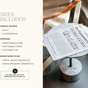 May include: A white marble table with a black metal stand, displaying a newspaper announcement with the headline "The Engagement Post EXTRA! EXTRA! Claire & James ARE ENGAGED". The announcement is printed on a white background with black text. The table is on a gray surface.