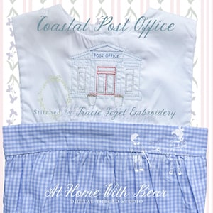 May include: White and blue embroidered baby outfit with the text "Coastal Post Office". The design features a post office building with a red door and flower pots. The bottom half is blue gingham.