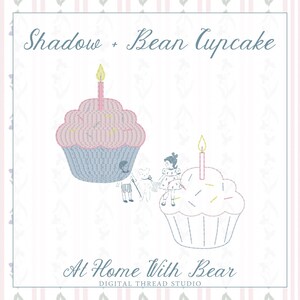 Op de afbeelding: Een borduurontwerp met twee cupcakes met brandende kaarsjes, één roze en één in omtrek, naast een kleine illustratie van twee kinderen en een teddybeer. De tekst luidt Shadow + Bean Cupcake en At Home With Bear Digital Thread Studio.