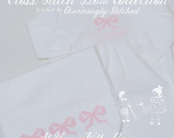 May include: White baby outfit set with pink cross-stitched bow details. The set includes a long-sleeved top with the name "Scarlett" embroidered and a matching blanket. Text on the image reads "Cross Stitch Bow Collection" and "At Home With Bear".