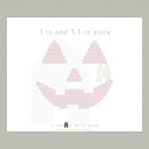 May include: A cross-stitch pattern of a jack-o'-lantern face in light pink, with the text "3 in and 3.5 in sizes" at the top. The design is on a white background, with the words "AT HOME WITH BEAR" at the bottom.