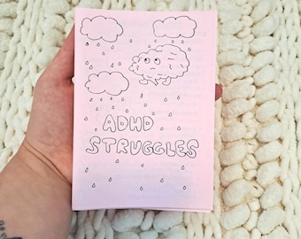 Puede incluir: Una tarjeta rosa con un cerebro de dibujos animados con una cara triste y gotas de lluvia que caen de las nubes. El texto "ADHD STRUGGLES" está escrito en negro en la tarjeta.