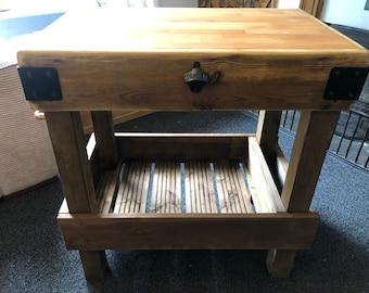 May include: Rustic wooden kitchen island with a butcher block top, a lower shelf, and a bottle opener. The island is made of reclaimed wood and has a natural finish.