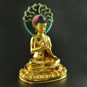 May include: Gold-coloured statue of a seated Buddha with a multi-headed serpent headdress. The Buddha is wearing a robe and has a serene expression. The statue is on a base with intricate details.