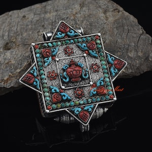 May include: A silver pendant with a square shape and intricate details. The pendant is decorated with turquoise and coral stones, and features a floral design.