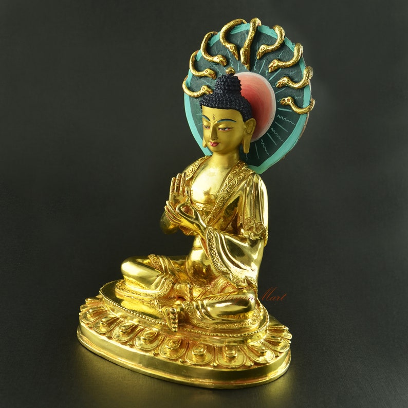 May include: A gold-coloured statue of Buddha with a multi-headed snake headdress. The statue is sitting in a meditative pose with hands in the gesture of meditation. The statue is on a gold-coloured base with intricate details.