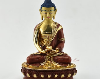 May include: A gold and red Buddha statue in a seated meditation pose. The statue is adorned with intricate details and is set on a lotus base.