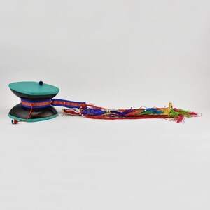 May include: A teal and black prayer wheel with a red, blue and gold tassel. The prayer wheel is a traditional Buddhist item used for meditation and chanting.