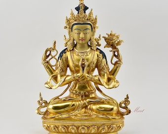 May include: A gold-colored statue of a four-armed deity, sitting in a meditative pose with hands in prayer position. The deity is adorned with intricate details and a crown. The statue is set on a lotus base.