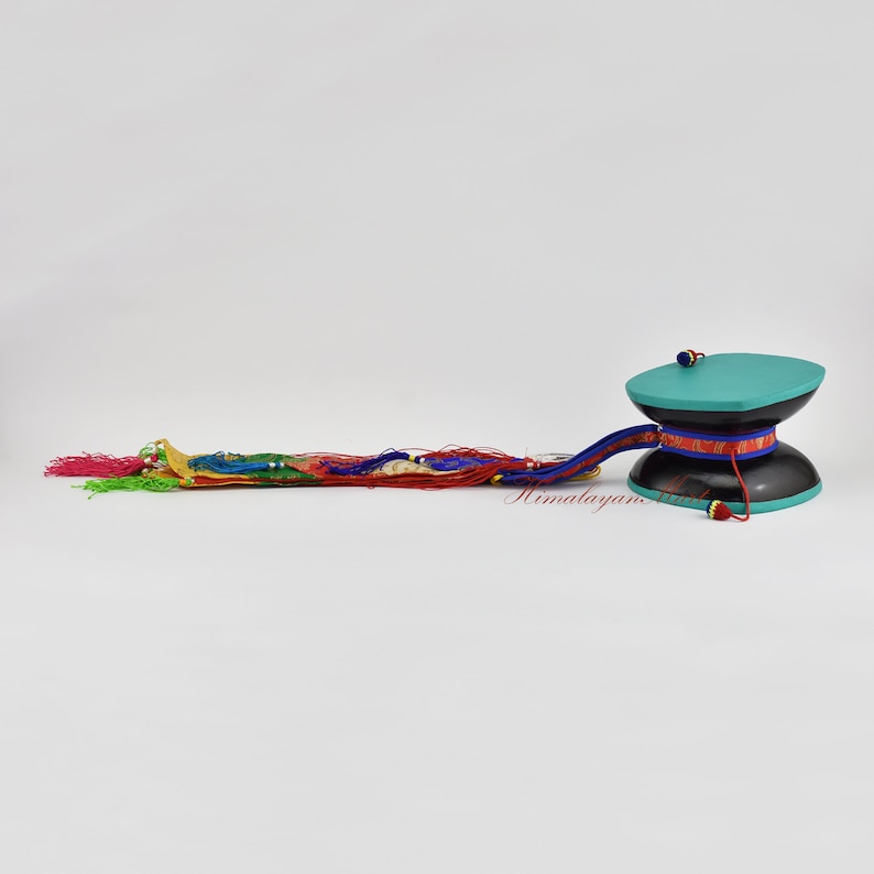 May include: A teal and black prayer wheel with a long, colourful tassel. The tassel is made of red, blue, green, yellow and white threads.