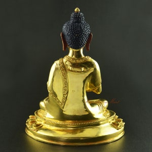 May include: A gold-coloured Buddha statue sitting in meditation pose. The statue has a detailed design and is made of metal. The statue is sitting on a circular base.