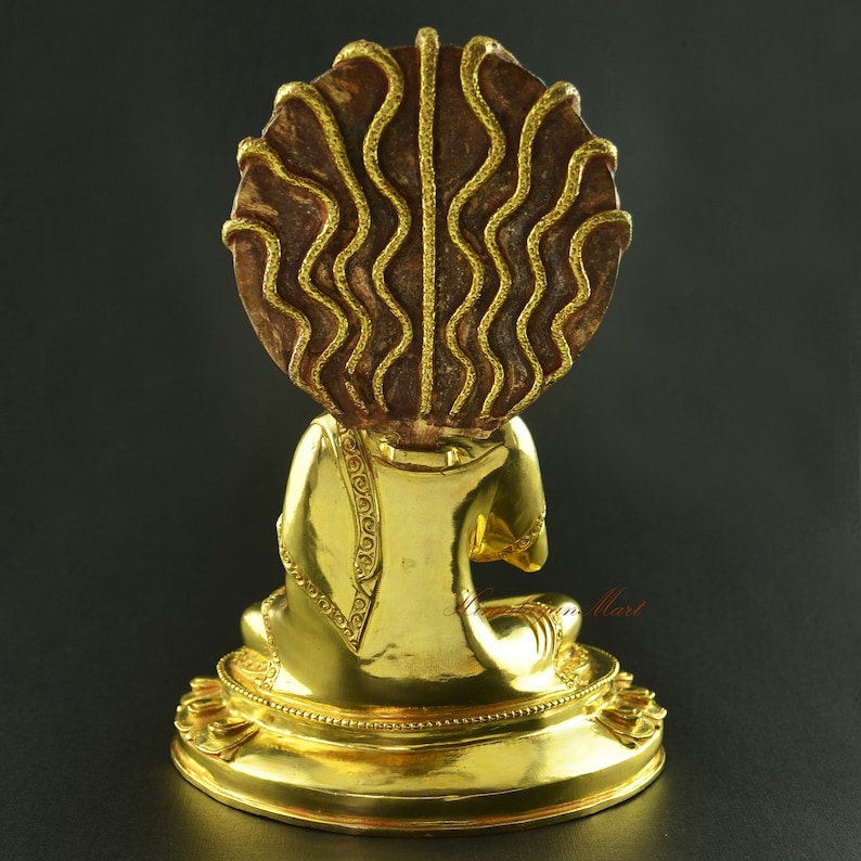 May include: A gold-coloured statue of a seated Buddha with a decorative, brown, circular headpiece. The headpiece has a wavy, textured design.