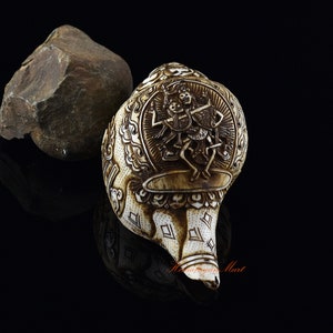 May include: A white conch shell with intricate carvings of a deity, surrounded by a decorative border. The shell is polished and has a smooth, glossy finish.