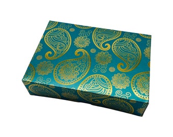 Könnte beinhalten: Eine rechteckige Geschenkbox mit türkisblauem Hintergrund und goldenem Paisley-Muster. Die Box hat eine glänzende Oberfläche und ist geschlossen. Das Paisley-Design umfasst Tropfenformen und florale Elemente.