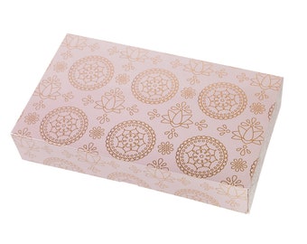 Könnte beinhalten: Eine rosa Geschenkbox mit einem goldenen Blumenmuster. Die Box ist geschlossen und die Oberseite ist sichtbar.