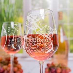 May include: Two wine glasses with a white etched design of the Boston, MA city map. The glasses are filled with rose wine and are sitting on a table with grapes in the background.