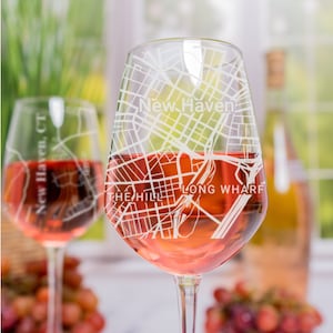 May include: Two wine glasses with a rose-colored wine. The glasses are etched with a map of New Haven, Connecticut, including the text "New Haven", "The Hill", and "Long Wharf".