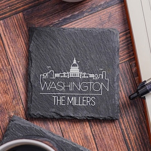 May include: Black slate coaster with a white outline of the Washington D.C. skyline and the text "WASHINGTON" and "THE MILLERS".