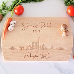 May include: A personalized wooden cutting board with a laser-engraved design of the Washington, DC skyline. The board is light brown and features the text "Justin & Rachel 11.26.21 Washington, DC".