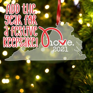May include: A clear acrylic Christmas ornament shaped like the state of Virginia. The ornament has a red ribbon and the text "Home. 2021" on it. The text "Add the year for a festive keepsake!" is printed on the ornament.